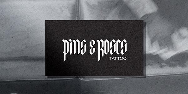 Black and white image featuring the "Pins & Roses Tattoo" logo on a textured background.