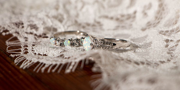 Two wedding rings with opal and diamond accents rest on delicate lace fabric.
