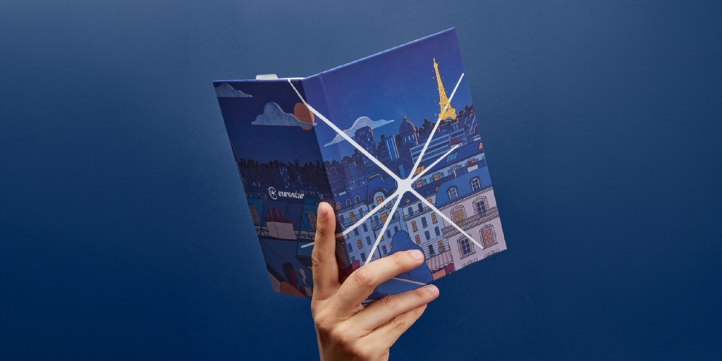 A hand holds a colorful booklet featuring a cityscape with the Eiffel Tower against a blue background.